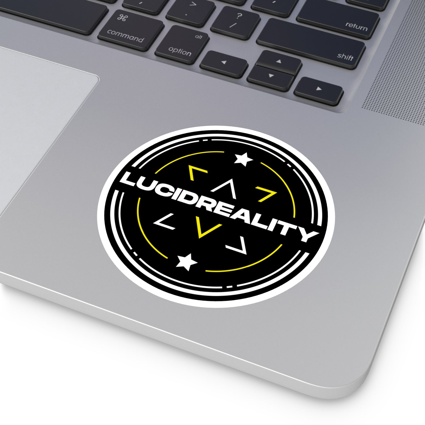Round Lucid Reality logo sticker applied to a laptop, showing the black shield design with white "LUCID REALITY" text.