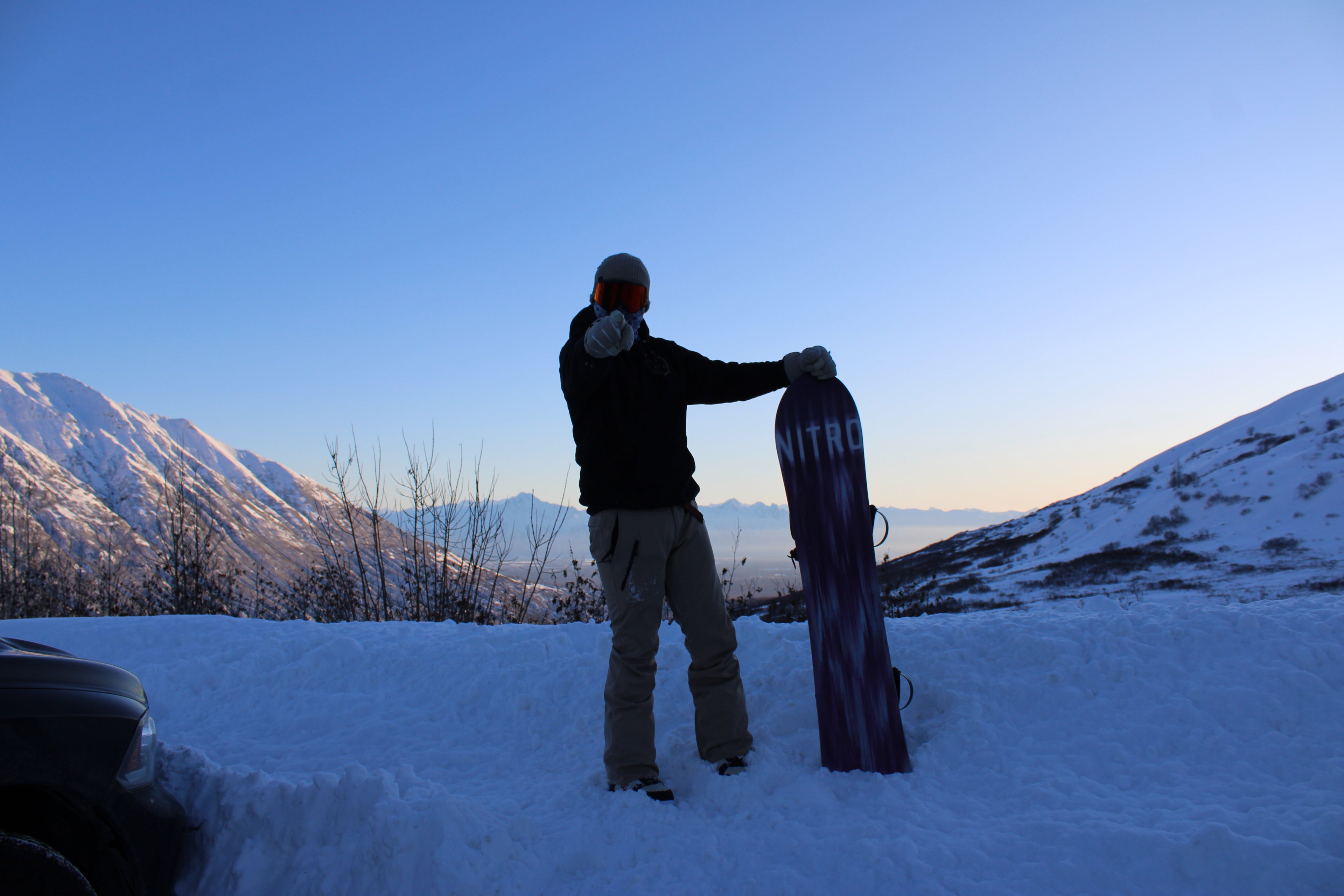 Person holding a snowboard in a snowy landscape with mountains in the background