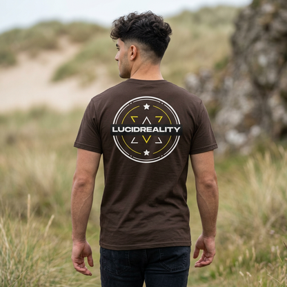 Man wearing the brown Lucid Reality Logo Tee in a grassy dune setting, showing the large circular shield logo on the back.