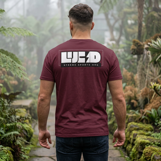 Man wearing the maroon Lucid Reality Lightning Bolt Tee in a misty forest setting, showing the white "LUCID" lightning bolt design on the back.