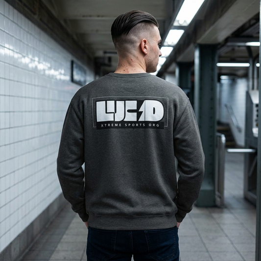 Man wearing the dark gray Lucid Reality Lightning Bolt Crewneck Sweatshirt in a subway station, showing the white "LUCID" lightning bolt design on the back.