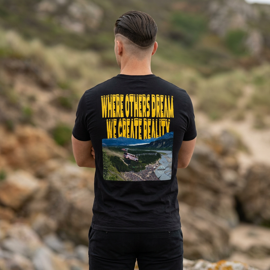 Athlete wearing the black Lucid Reality Where Others Dream Tee, back view showing the "Where Others Dream We Create Reality" graphic with mountain and river landscape, framed against a rocky outdoor backdrop.
