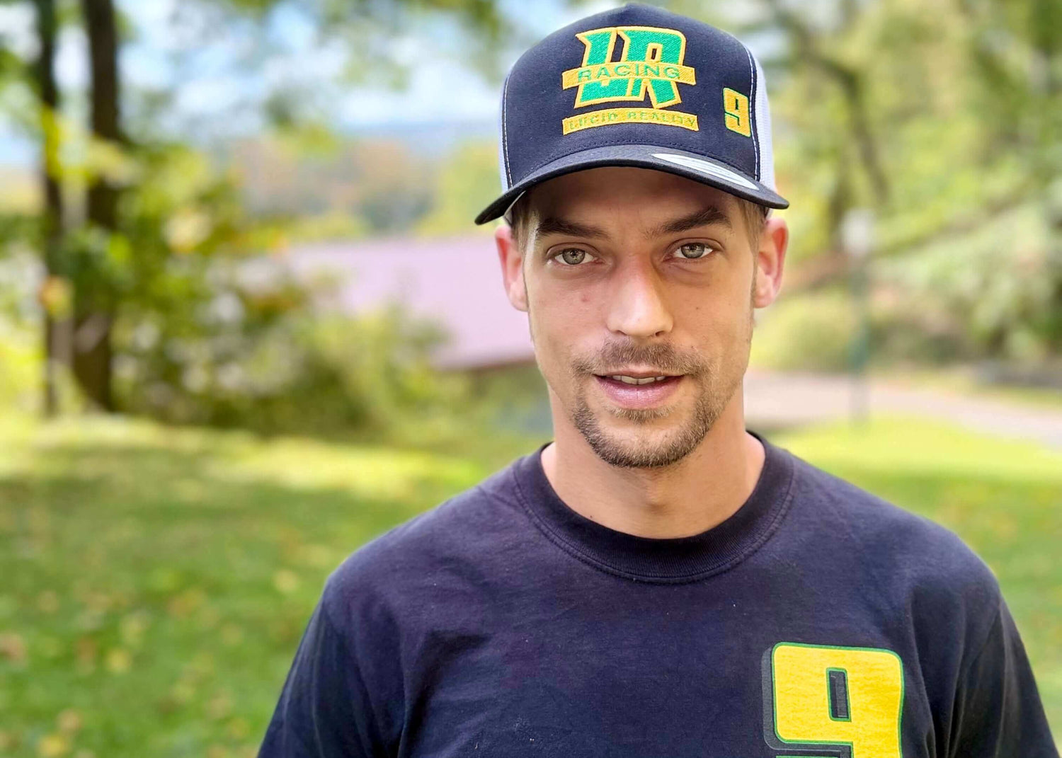 Man wearing a navy cap with yellow text and a matching navy t-shirt with yellow number 9 outdoors.