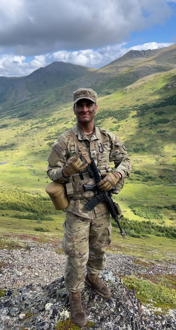 Person in military uniform with gear standing in a mountainous landscape